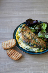 Frittata with chicory and cheese, served with oakleaf lettuce salad and toasted bread. Selective focus.
