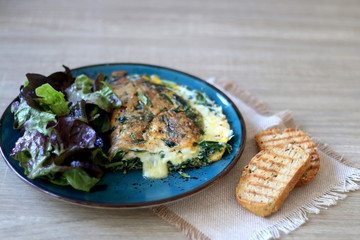 Frittata with chicory and cheese, served with oakleaf lettuce salad and toasted bread. Selective focus.
