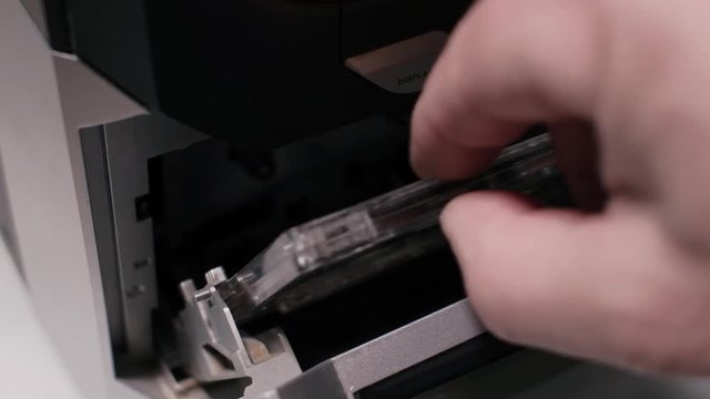 Side close up detail shot, man dj turn the page of cassette in old vintage analogue tape recorder or hifi stereo, dark low light contrast scene, 4H UHD