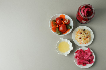 a set of fermented food great for gut health - top view of glass bowls and plate on gray background: sauerkraut, pickled cabbage with beetroot, pickled cucumbers, carrots and tomatoes