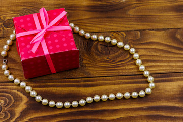 Gift box and pearl necklace on wooden background