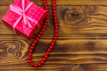 Gift box and red beads necklace on wooden background