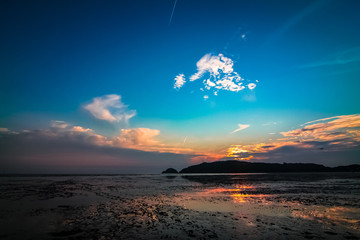 Far-away view of a muddy shore reflecting blue and orange gradient sky with dramatic sunset