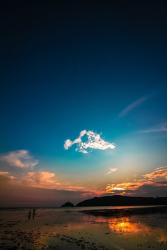 Far-away view of a muddy shore with children running and blue and orange gradient sky with dramatic sunset