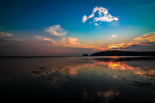 Far-away view of a muddy shore reflecting blue and orange gradient sky with dramatic sunset
