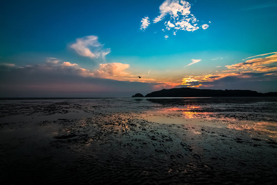 Far-away view of a muddy shore reflecting blue and orange gradient sky with dramatic sunset