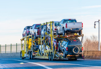 Big rig yellow car hauler semi truck transporting cars on two levels semi trailer driving on the...