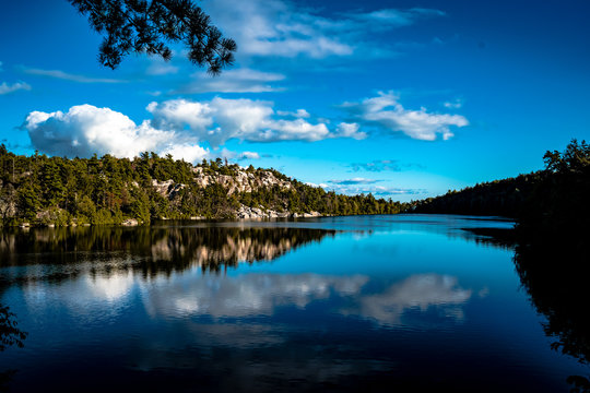Long lake with rocky cliff face on left side and forest on the right with blue sky