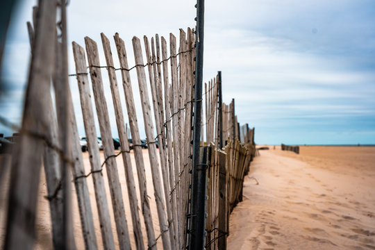 Wooden fence at beach with cars, ocean, and sand in background