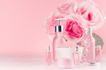 Bath cosmetics products, romantic bouquet, accessories in elegant pastel pink color - massage rose oil, bath salt, cream, soap, perfume, towel on white wood board.