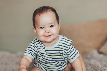 Beautiful smiling baby girl with big dark eyes dark hair sitting at floor and looking up at camera