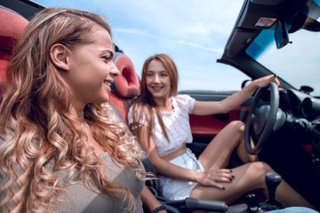 smiling girlfriends traveling in a convertible car.