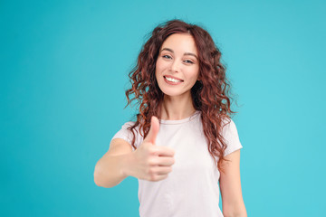Attractive brunette girl with curly hair isolated over blue turquoise background happy and showing thumbs up