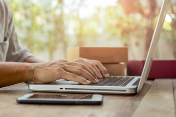 Man hands typing on laptop keyboard with parcel package delivery on table.