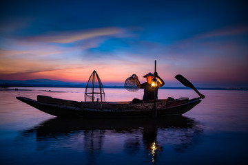 Traditional asia fisherman with using a bamboo square dip net on wooden boat at beautiful morning...