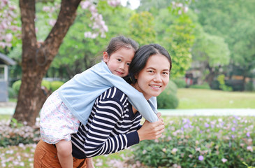 Fototapeta premium Happy mother carrying her daughter in garden with fully fall pink flower around. Happy loving family.