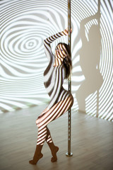 A beautiful woman stands at the pole in the light of the projector. Young sexy slim woman pole...