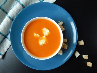 Pumpkin cream soup on a blue plate with cream cheese and croutons on a black background