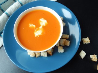Pumpkin cream soup on a blue plate with cream cheese and croutons on a black background