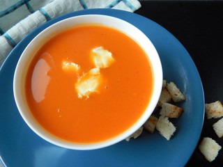 Pumpkin cream soup on a blue plate with cream cheese and croutons on a black background