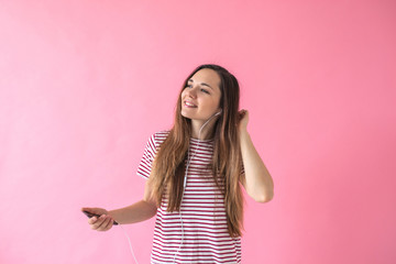 Positive joyful girl on a pink background listening to music.