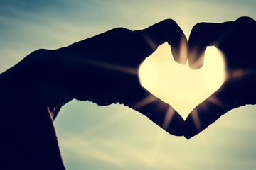 Two hands making a heart shape in the sky with blue sky with clouds in background