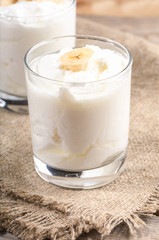 Traditional homemade yogurt with banana slices in transparent glasses on burlap napkin. 