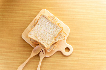 Whole wheat bread is stacked on a wooden cutting board placed on a Wooden table. Homemade sandwich breakfast preparing. Cooking ingredient. Food background concept with copy space.