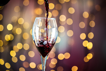  Pouring red wine into the glass. Golden bokeh background.