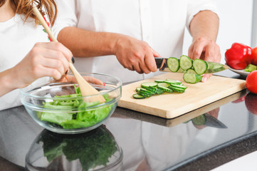 family cooking together man cutting cucumber and woman blending lettuce leaves