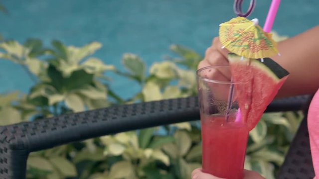 Tanned Girl In Pink Shirt Rests Near Swimming Pool With Blue Water And Drinks Pink Watermelon Cocktail