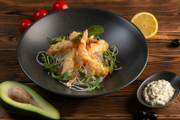 Tempura shrimps with tartar sauce on a black plate on a wooden background