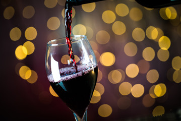 Obraz na płótnie Canvas Pouring red wine into the glass. Golden bokeh background.