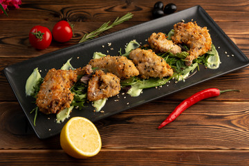 Pieces of chicken in batter on a black rectangular plate on a wooden background
