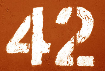 Number 42 in stencil on rusty metal wall in orange tone.