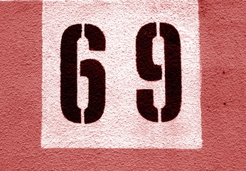 Number 69 on cement wall in stencil in red tone.