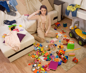 Mother sitting on the couch. Mom tired to tidy up the house. Child scattered toys. Children's room. Mess in the house