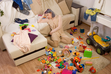 Mother sitting on the couch. Mom tired to tidy up the house. Child scattered toys. Children's room. Mess in the house