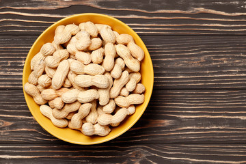 Bowl full of roasted peanuts on a brown wooden background with place for text.