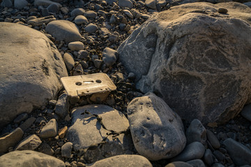 An old music cassette, seen between the stones of Llantwit Major Beach, Vale of Glamorgan, South Glamorgan, Wales, UK