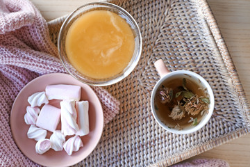 Wicker tray with cup of tea, honey and sweets on table