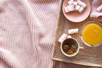 Wicker tray with cup of tea, honey and sweets on plaid