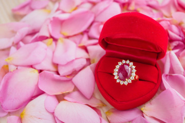 elegant ruby ring in red heart jewelry box on beautiful pink rose petal background close up