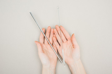 partial view of woman holding cleaning brush and stainless steel straw in hands on grey