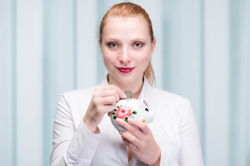 young red haired woman puts a coin into her piggy bank