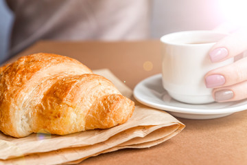 Female hands with manicure holding cup of coffee and eating croissant. Breakfast in french style