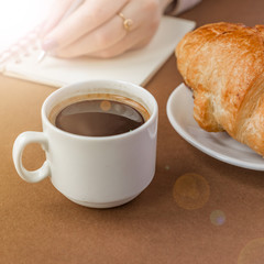 Close up of croissant and espresso. Woman writing on notebook . Freelancer at work