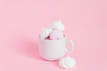 White and pink twisted meringues in a small porcelain coffe cup on pink background. French dessert prepared from whipped with sugar and baked egg whites. Greeting card with copy space