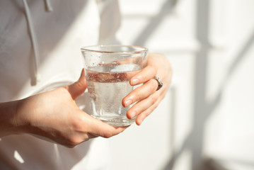 Close-up girl hands in the office stands in the sunlight holding a glass of clean water in between work