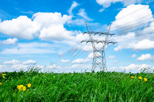 Energy infrastructure. High voltage power line. Green energy concept. Electricity pylon and power line on a blue sky and green grass background. 